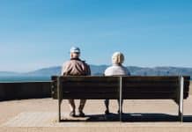 man and woman sitting on bench facing sea