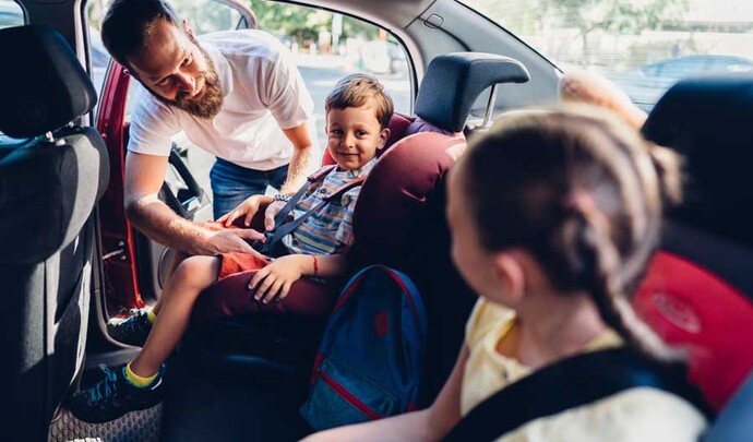 un homme attache un enfant avec la ceinture de sécurité à l'arrière d'une voiture
