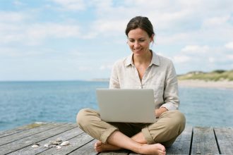 Femme assise sur une terrasse face à la mer avec son ordinateur